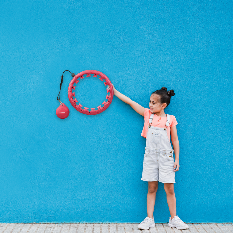 A girl is standing with a red hula hoop in her right hand